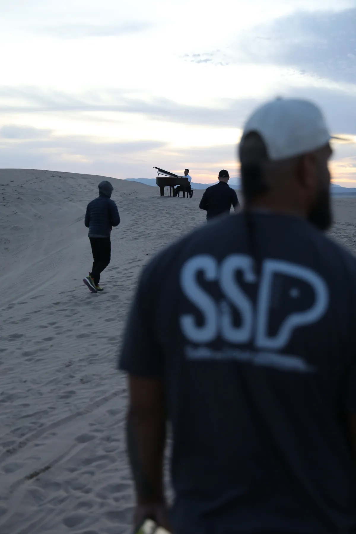 Mote, co-owner of Safe and Sound Pianos, walking the Little Sahara dunes during a music video piano shoot at twilight.