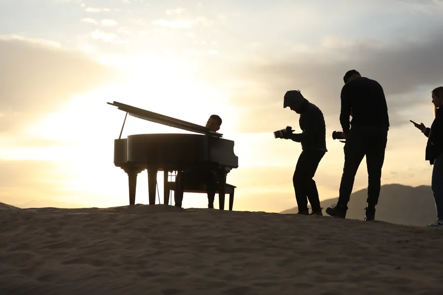 Behind the scenes: a pianist plays as photographers and crew work the shot at Little Sahara, sunset behind them.