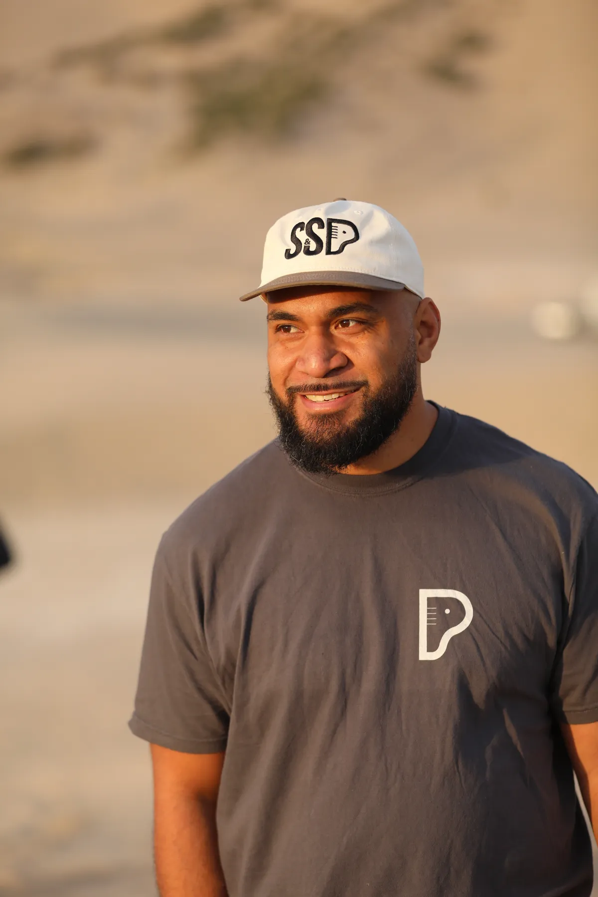 Mote, co-owner of Safe and Sound Pianos, smiling in branded SSP cap and shirt during a music video shoot.