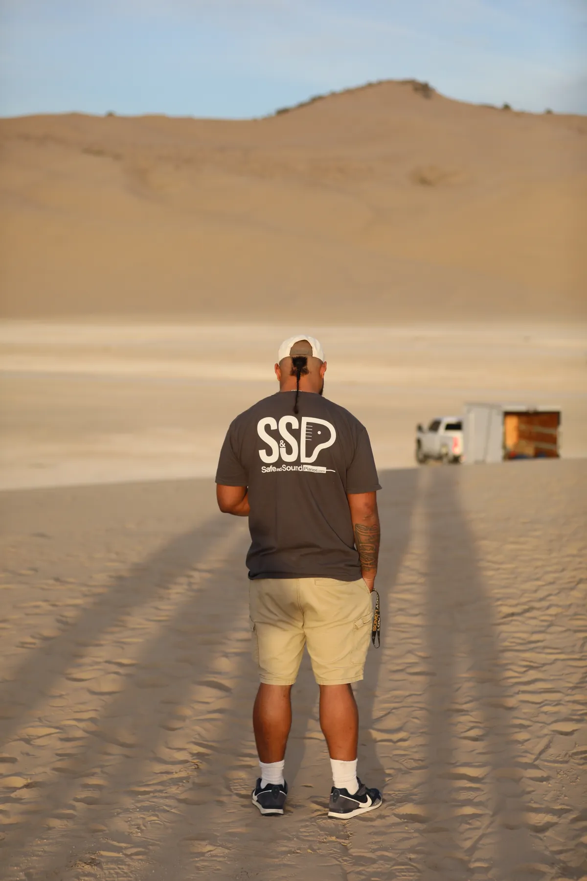 Mote walking on Little Sahara dunes in a Safe and Sound Pianos branded shirt during a music video shoot.