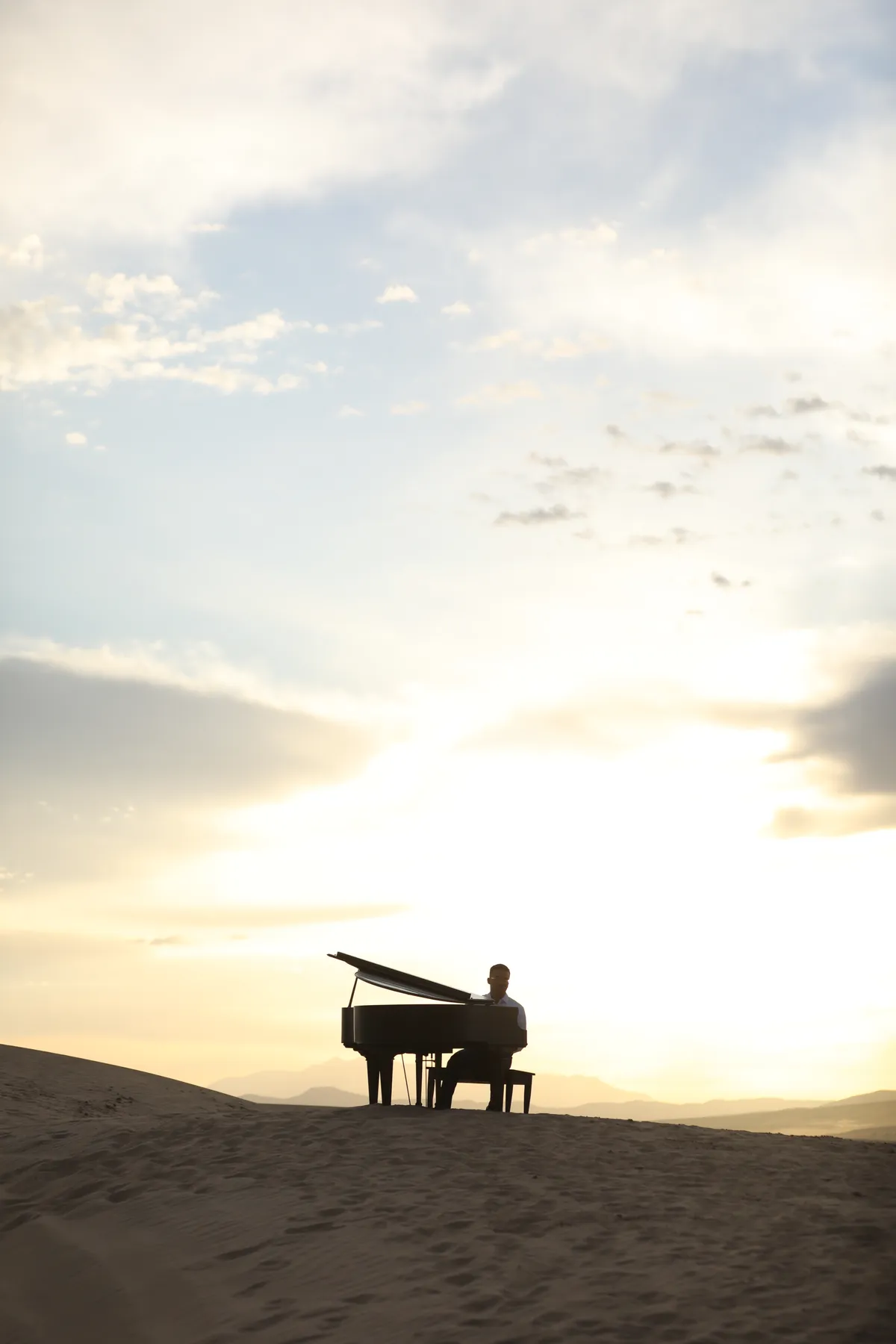 Silhouette of a piano and a figure on Little Sahara sand dunes against a luminous sunset.