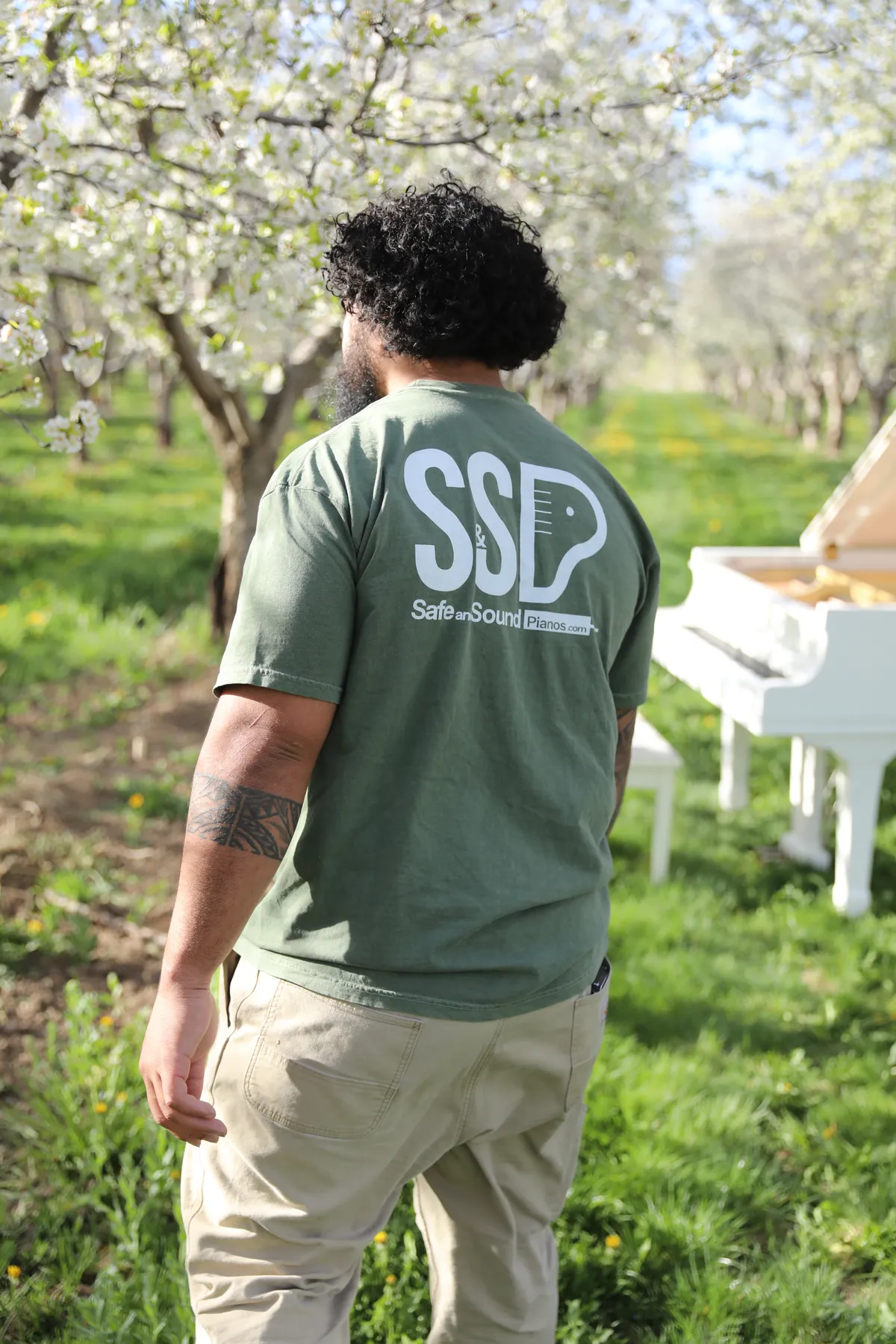 Mote in a Safe and Sound Pianos branded shirt with a Santaquin orchard in bloom behind him.