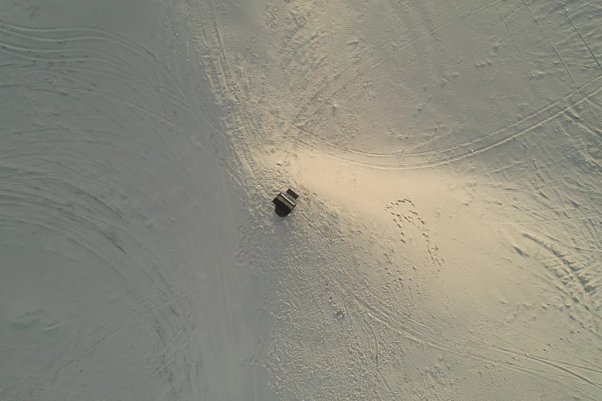 Drone's-eye view of an upright piano placed alone on the Little Sahara sand dunes from directly above.