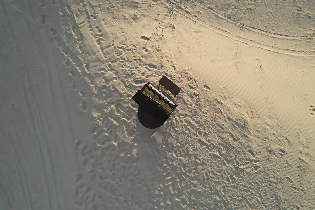 Aerial view of a grand piano on Little Sahara sand dunes — drone shot from directly overhead.