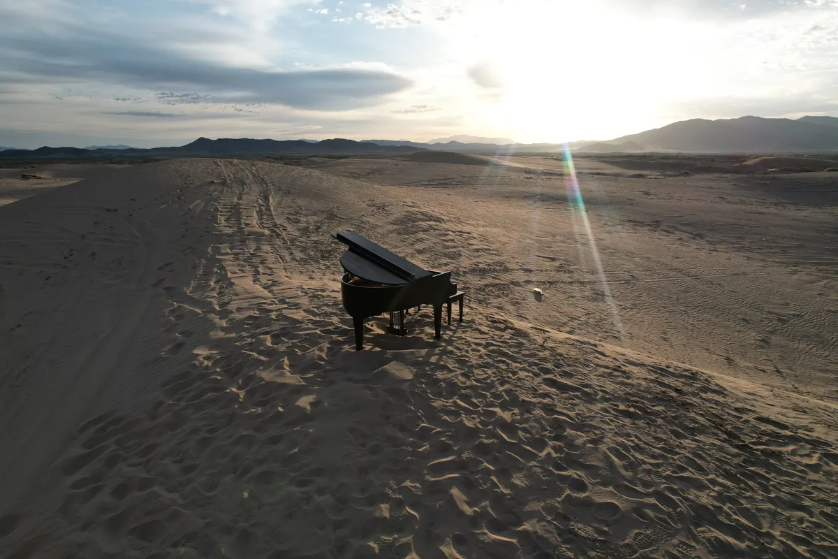 Sweeping aerial of Little Sahara sand dunes at sunset with a black grand piano in the foreground.