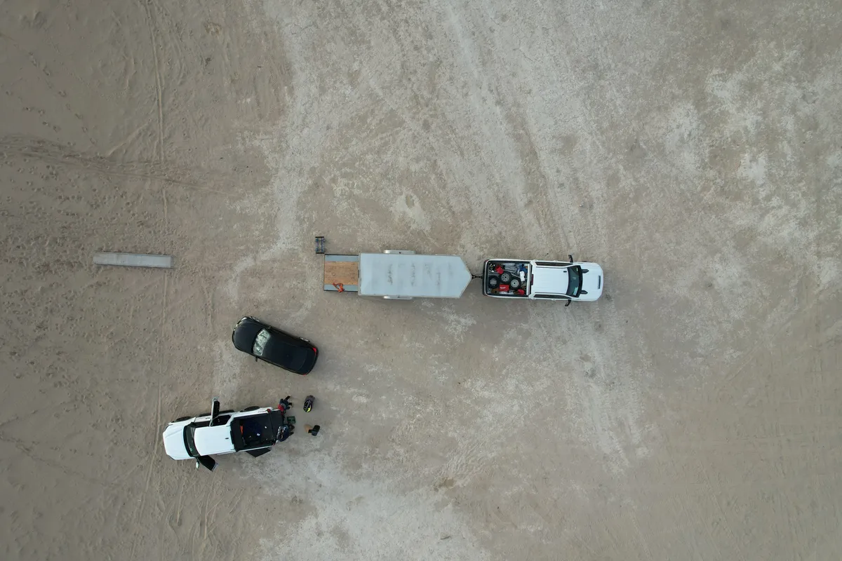 Drone overhead view of Safe and Sound Pianos' truck and trailer parked alongside another vehicle on the dunes during a music video shoot.