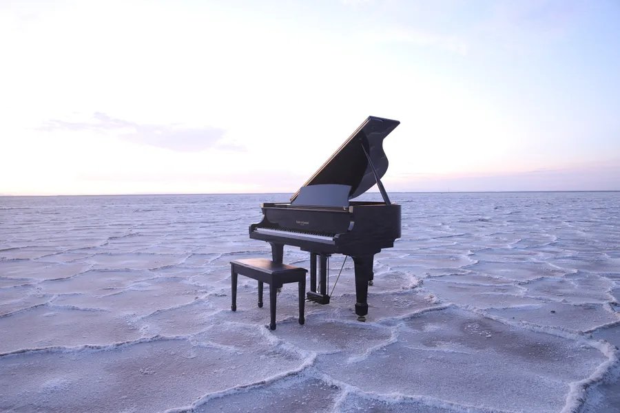A black grand piano staged on the hexagonal salt patterns of the Bonneville Salt Flats in Utah at twilight.