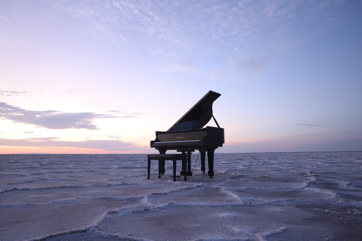 Black grand piano alone on the Bonneville Salt Flats, sunset clouds stretching across an endless horizon.