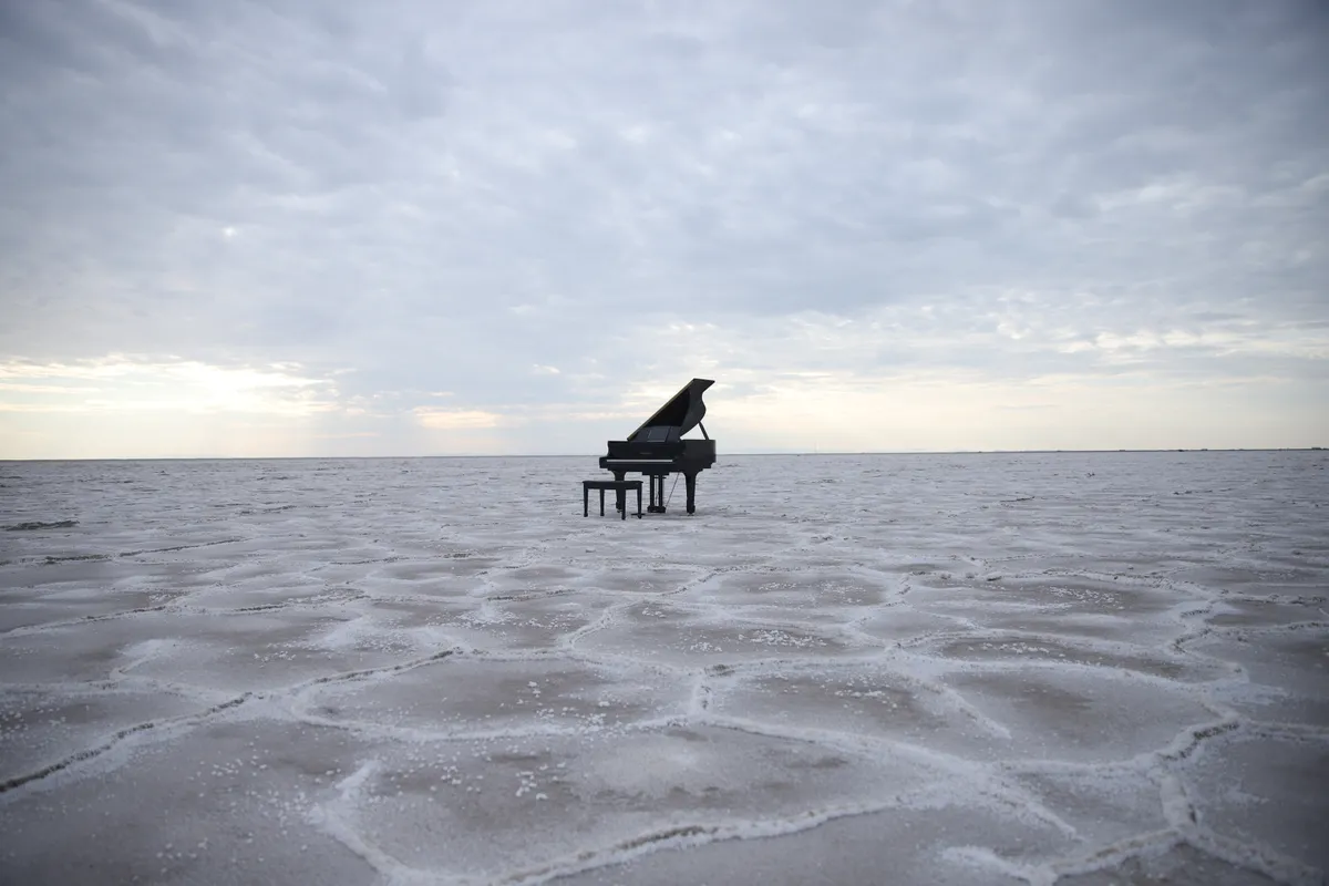Wide view of a black grand piano dwarfed by the vast Bonneville Salt Flats stretching to the horizon.