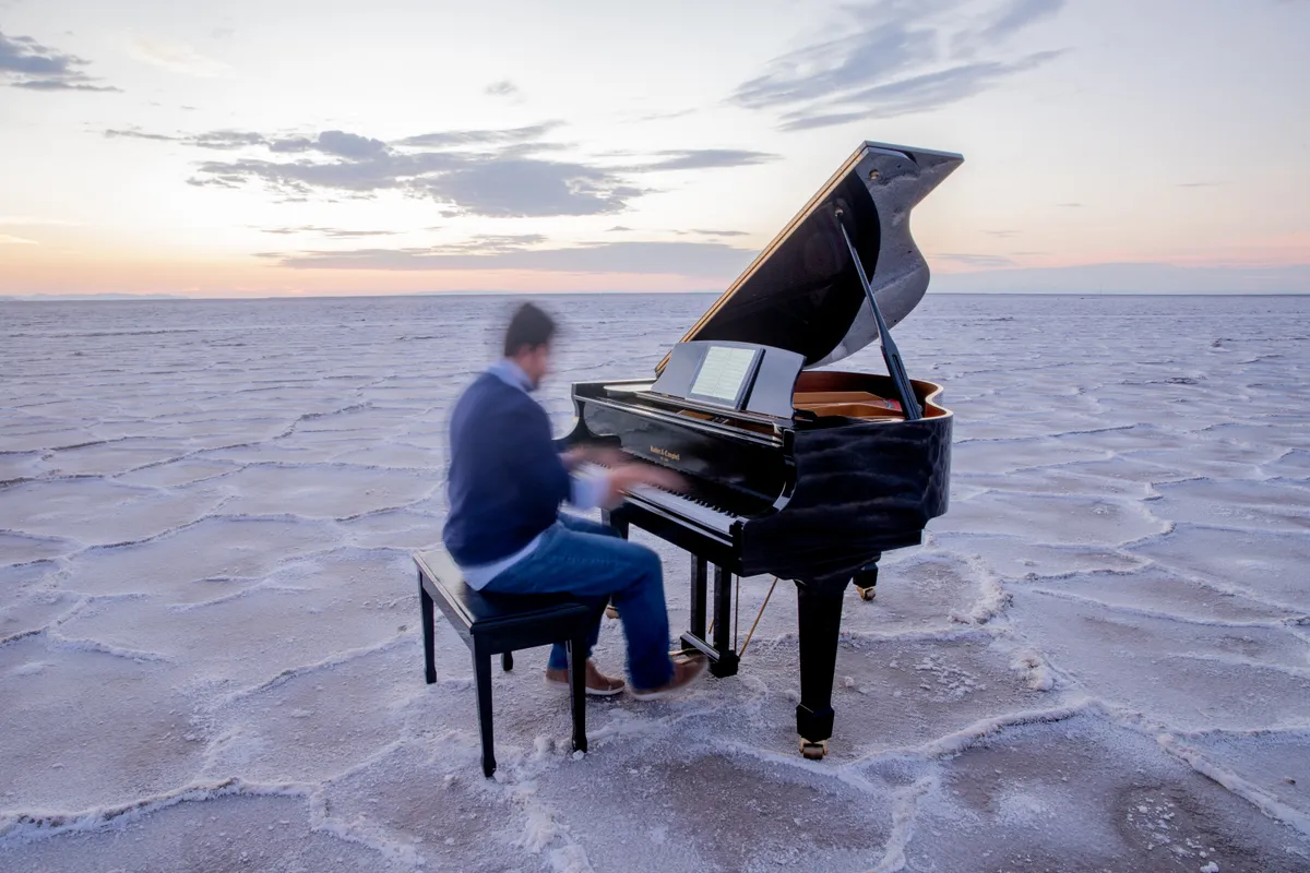 Sunset on the Bonneville Salt Flats with a pianist at a grand piano and a woman in a red dress nearby — a Safe and Sound Pianos rental for a Utah music video.