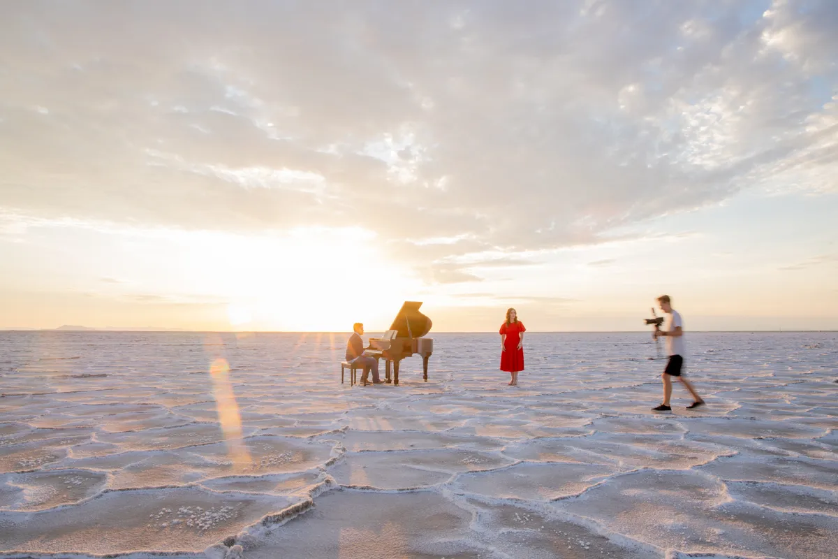 Minimalist composition: a tiny grand piano on the cracked surface of the Bonneville Salt Flats under a pale sky.