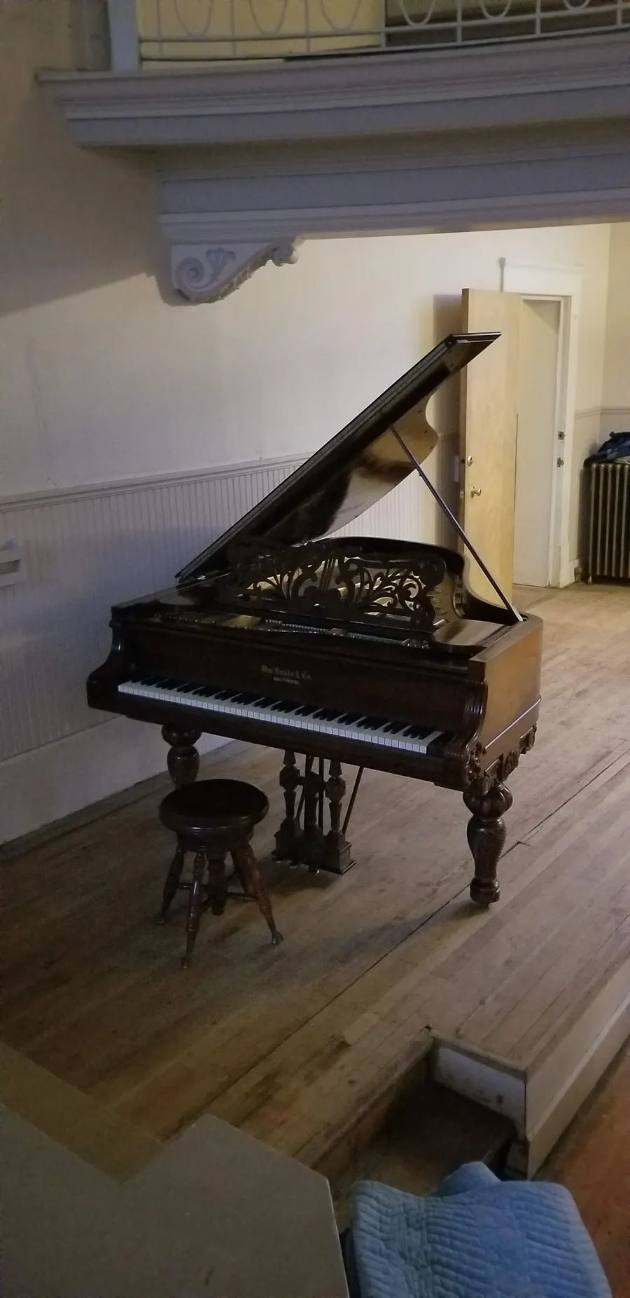 A vintage grand piano with intricate cabinet work in a historic hall, recently delivered by Safe and Sound Pianos.