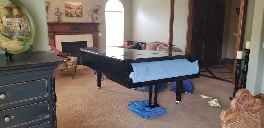 A wrapped grand piano staged in a residential living room, blankets and straps in place before the move.