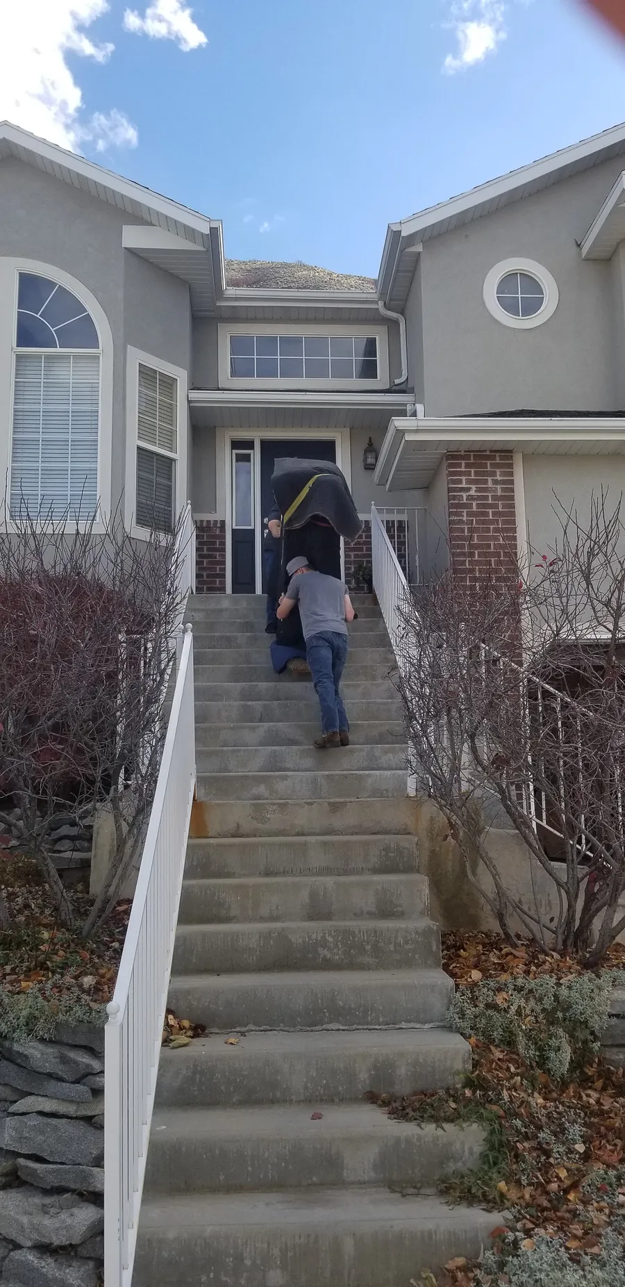 Crew carrying a wrapped piano up the exterior front steps of a Utah home in autumn.