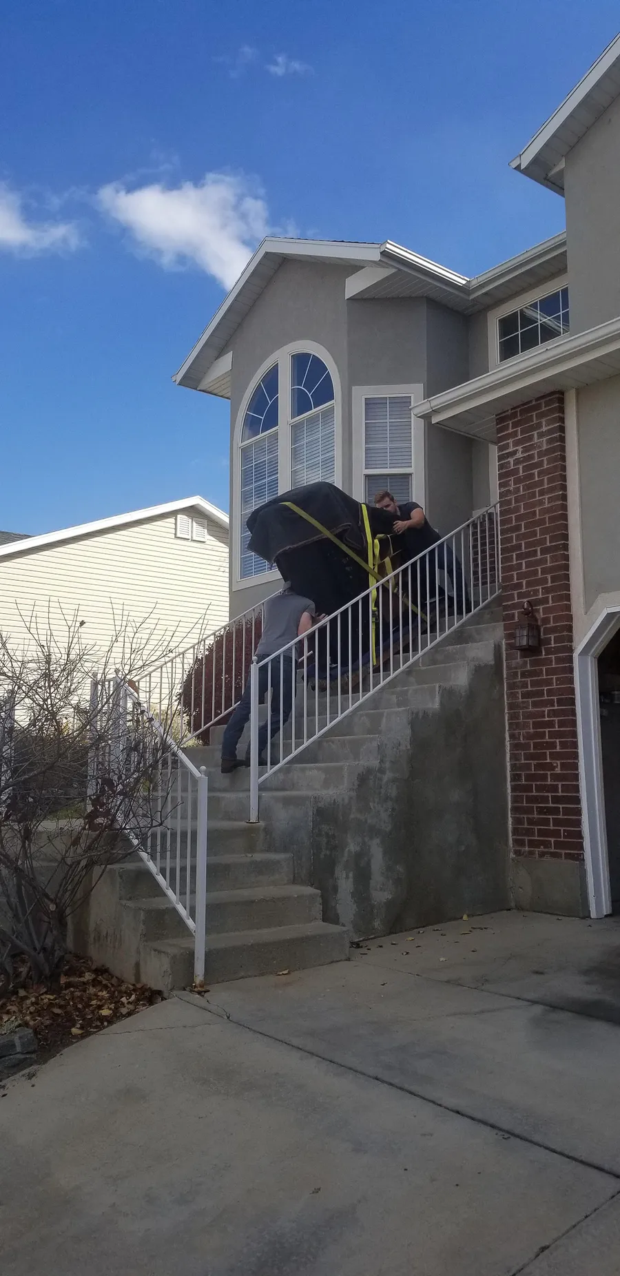 Safe and Sound Pianos crew carrying a wrapped piano up exterior steps to a Utah home.