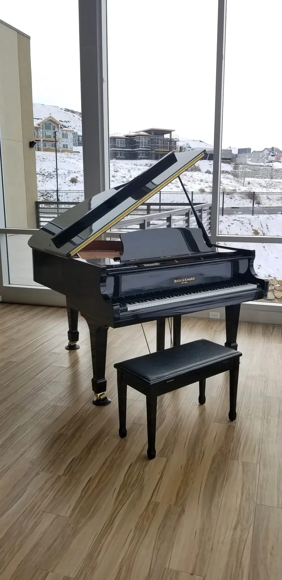 Black grand piano placed beside floor-to-ceiling windows overlooking the snow-covered Salt Lake Valley.