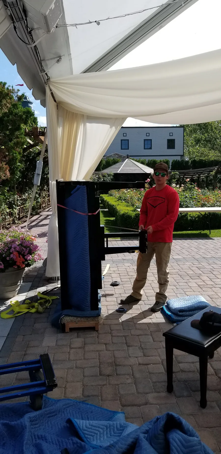 A crew member in a Safe and Sound Pianos shirt setting up a wrapped piano under an outdoor wedding tent in Utah.