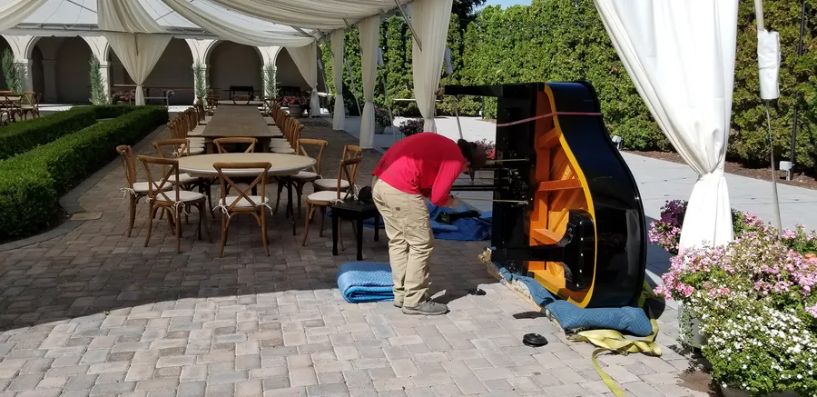 Safe and Sound Pianos crew adjusting the legs of a grand piano at an outdoor wedding venue.