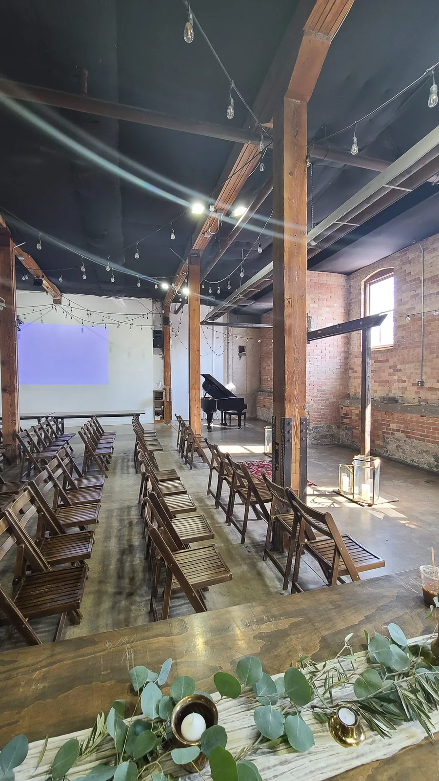 Wide view of a black grand piano in an industrial brick venue — a Safe and Sound Pianos rental delivery.