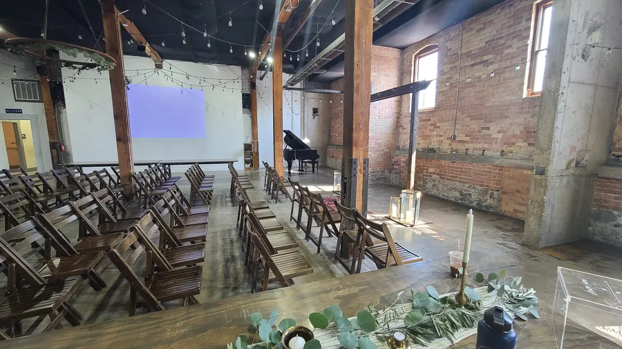 Black grand piano with brick walls and reclaimed beams behind it — a Utah event-venue placement.